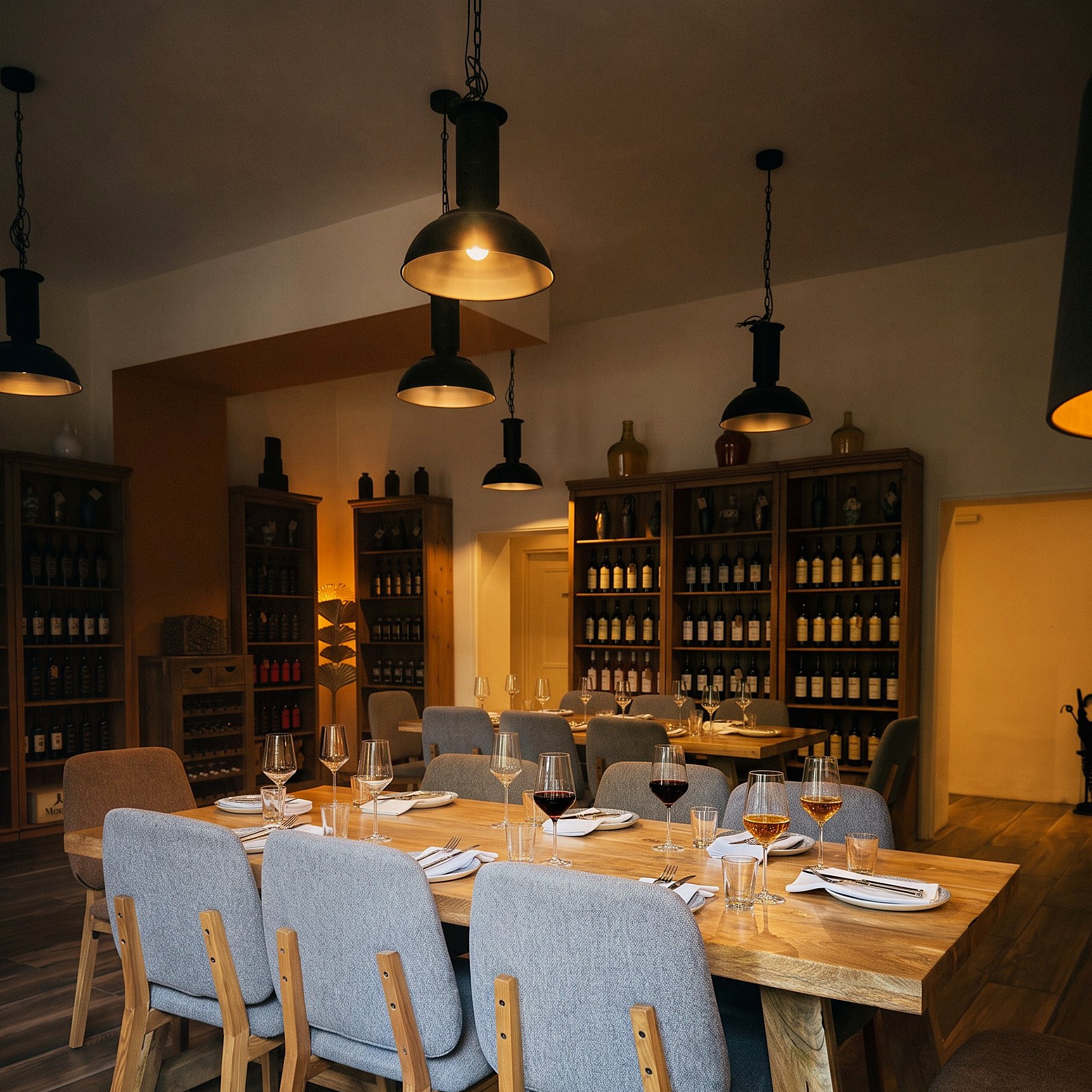 Der lange Tisch über die ganze Länge für eine Gesellschaft eingedeckt, Wein eingeschenkt, dahinter die Flaschenregale